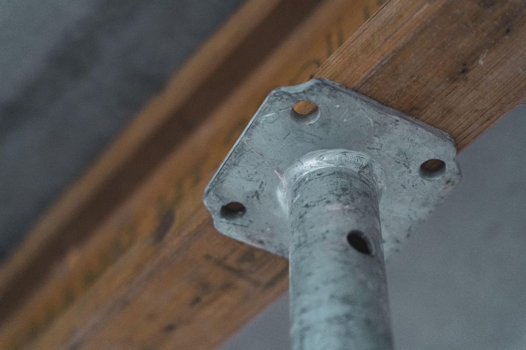 Nahaufnahme einer verzinkten Gerüstverbindung an einer Holzbohle