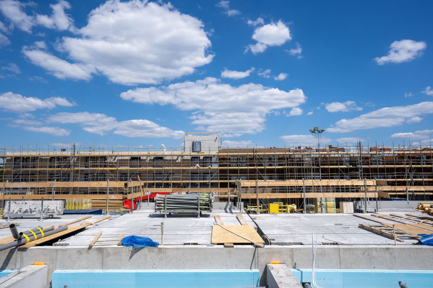 Langes Fassadengerüst mit Bohlenbelag an einem Neubau vor blauem Himmel