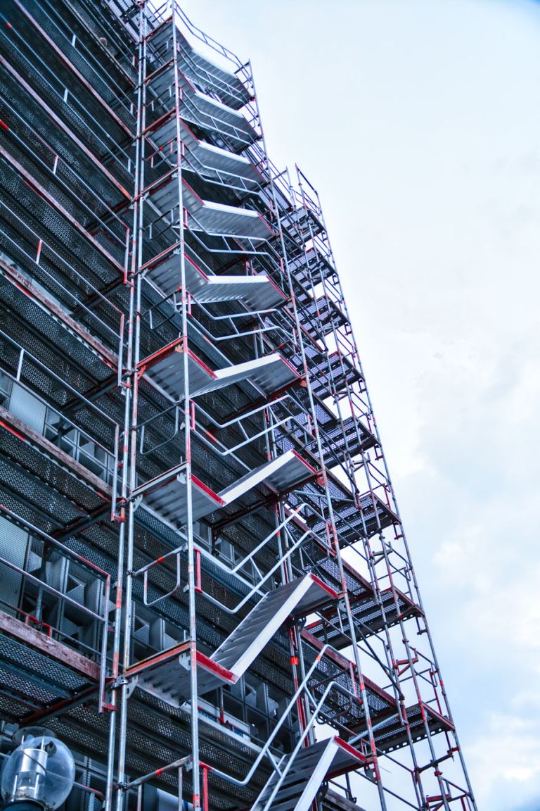Treppenläufe eines Gerüsts an einer hohen Fassade, von unten fotografiert