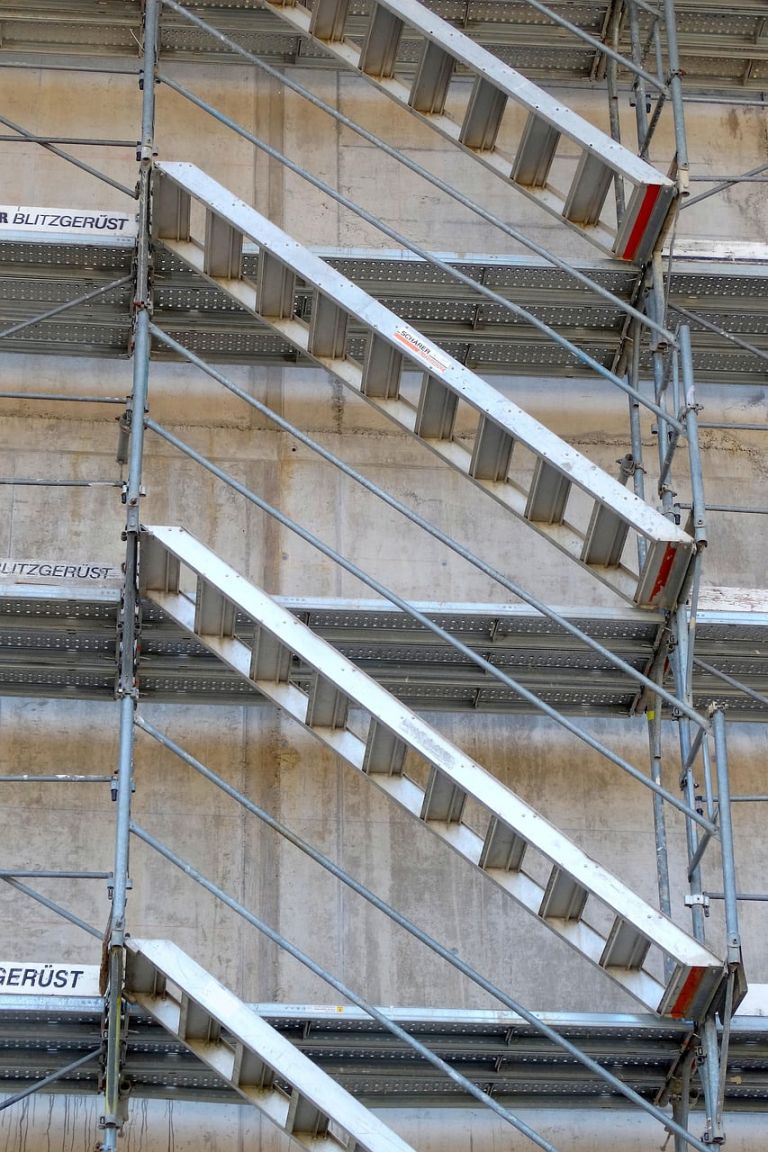Gegenläufige Gerüsttreppen vor einer Betonwand